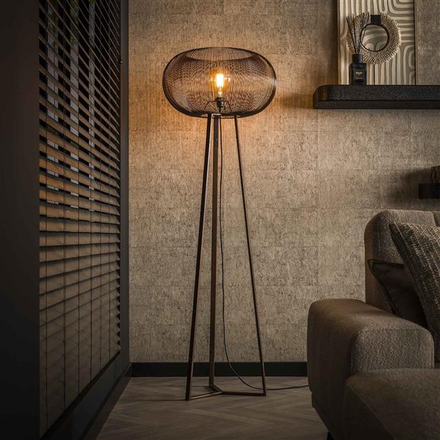 Industriële woonkamer met de focus op e Industriële vloerlamp van zwarte metalen poten en een metalen ronde lampenkap er op waar het licht doorheen schijnt.