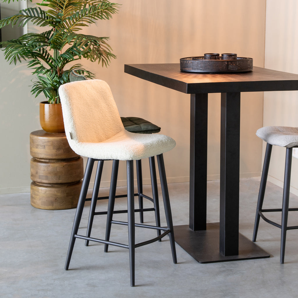 Zachte witte barkrukken met zwart metalen poten en een bartafel van zwart metaal in een modern interieur.