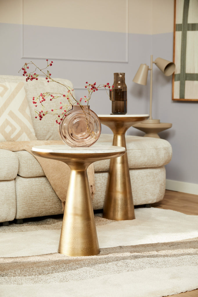 Marmeren bijzettafel met gouden onderkant in een modern interieur met zachte kleuren en stoffen.