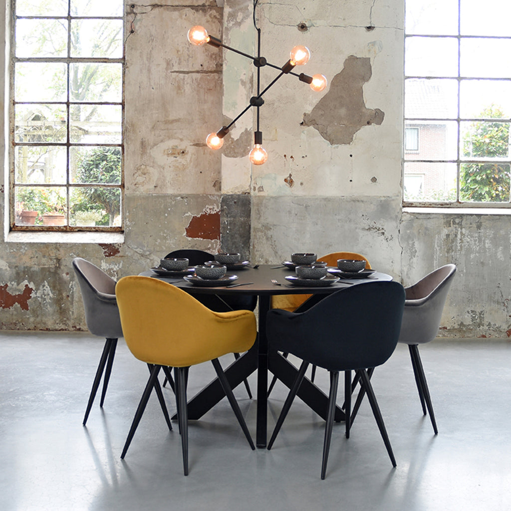 Een industriële eethoek met een ronde zwarte eettafel en zes stoelen in verschillende kleuren, boven de tafel hangt een Industriële hanglamp van zwart metalen stokken met blote gloeilampen aan de punten.