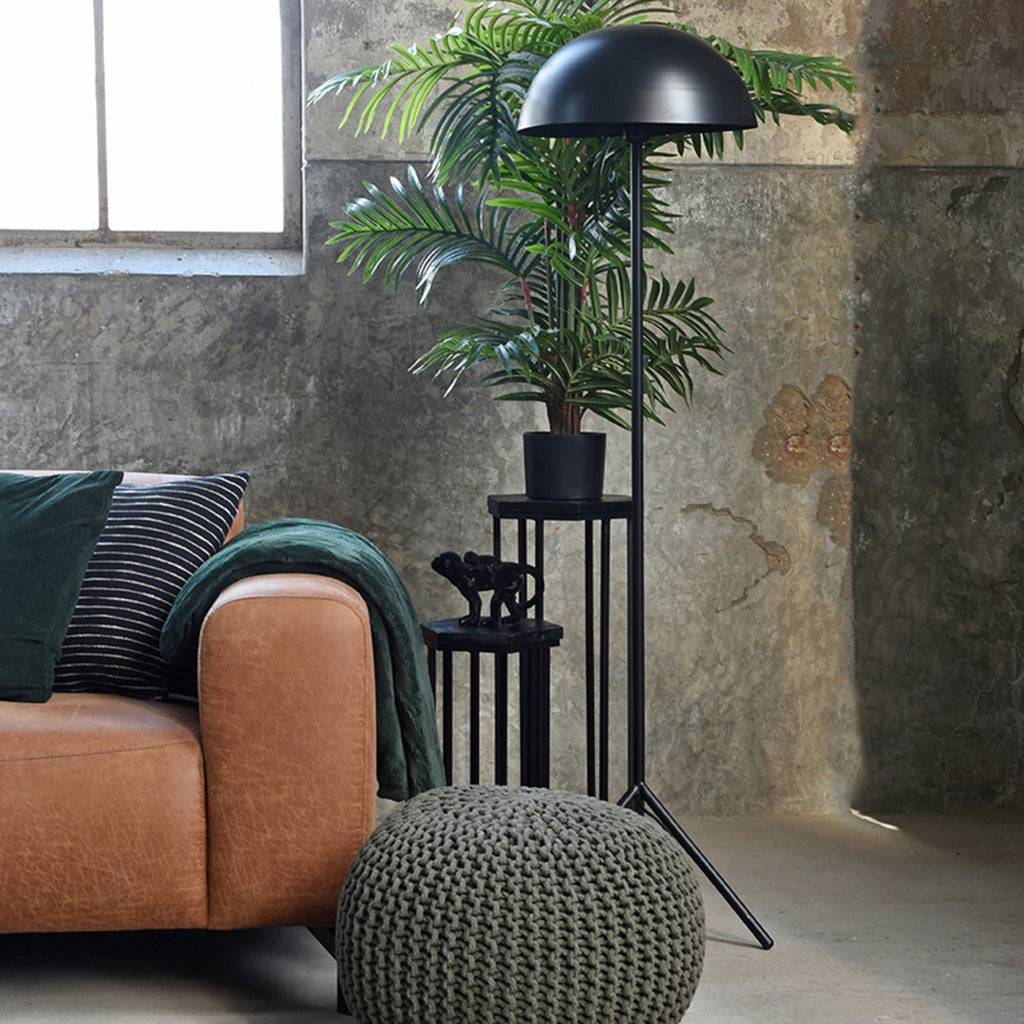 Industriële woonkamer met de focus op een Industriële dunne zwarte lamp naast een bruine leren bank met zwarte bijzettafels en een grijze poef er voor.