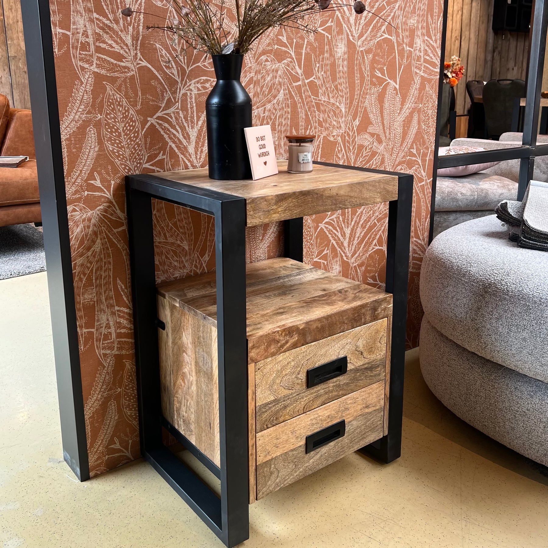 Een industrieel sidetable met wat decoraties er op naast een bank in een showroom.