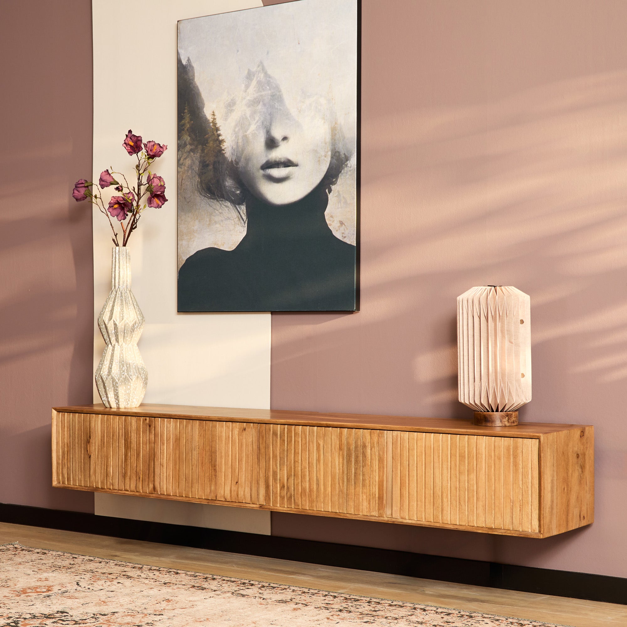 Zwevend tv meubel 220 cm van mangohout aan een roze muur met een schilderij.
