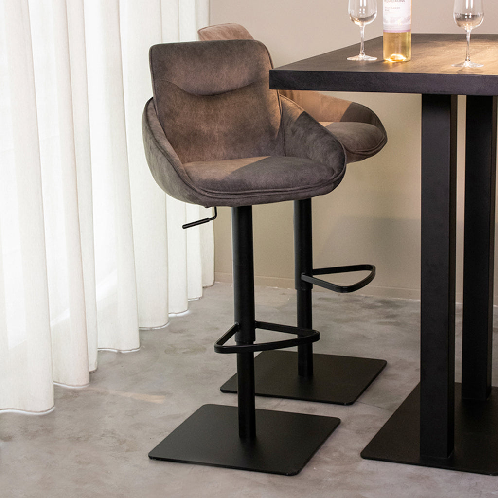 Draaibare grijze stoffen barkruk met zwart metalen poot naast een zwarte bartafel in een moderne eethoek.