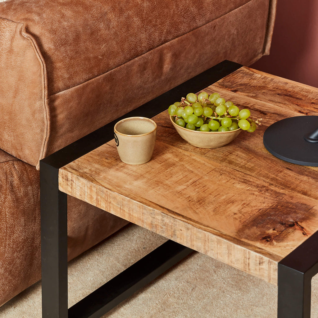Vierkante bijzettafel van mango hout en zwart metaal in simpel minimalistische stijl naast een brijn leren bank.